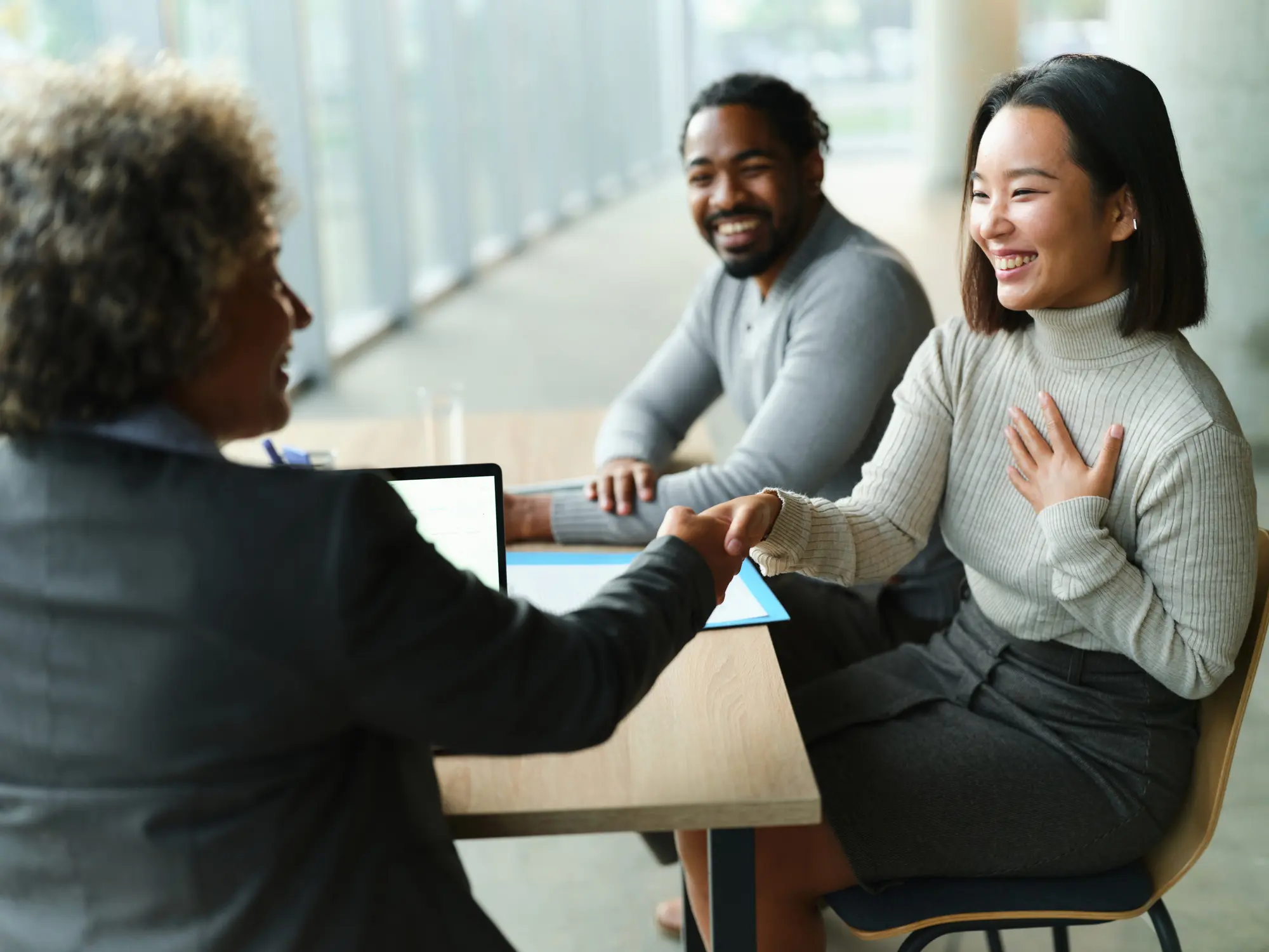 Happy diverse couple reached a successful deal with their insurance agent during a meeting in the office. Focus is on Chinese woman. Photographed in medium format.